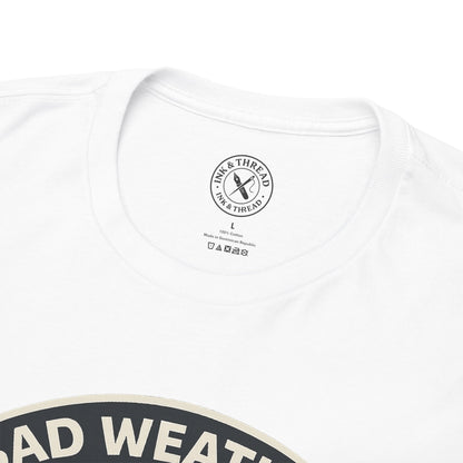 Close-up of Ink and Thread UK branded inner neck label on white t-shirt with Bad Weather Builds Character camping graphic design and care instructions