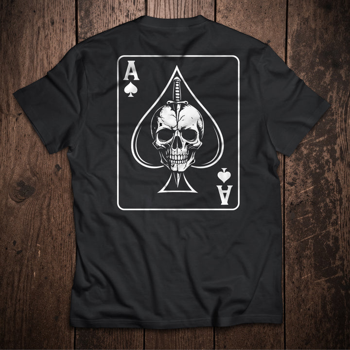 Black t-shirt flat lay on wooden surface with Ace of Spades playing card design featuring skull and dagger illustration
