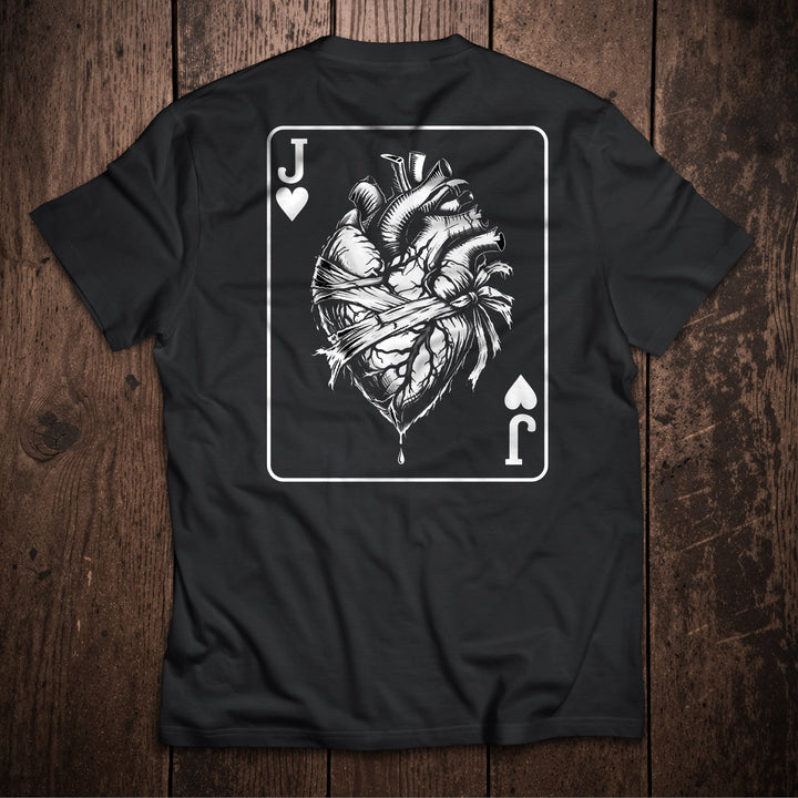 Black t-shirt flat lay on wooden surface with Jack of Hearts playing card design featuring anatomical heart illustration