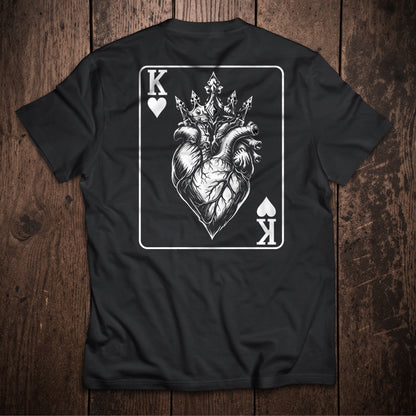 Black t-shirt flat lay on wooden surface with King of Hearts playing card design featuring crowned anatomical heart illustration