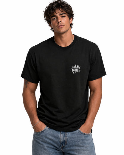Male model wearing black t-shirt with Ink and Thread script logo on left chest against white background