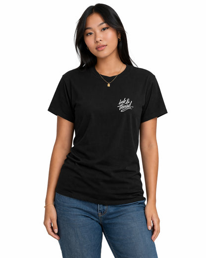 Female model wearing black t-shirt with Ink and Thread script logo on left chest against white background