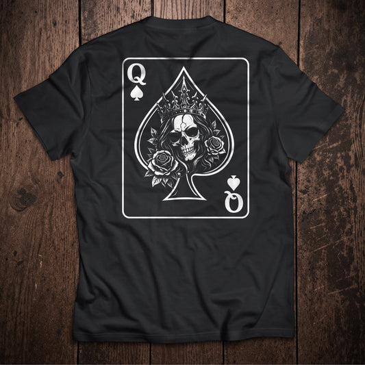 Black t-shirt flat lay on wooden surface with Queen of Spades playing card design featuring crowned skull with roses illustration