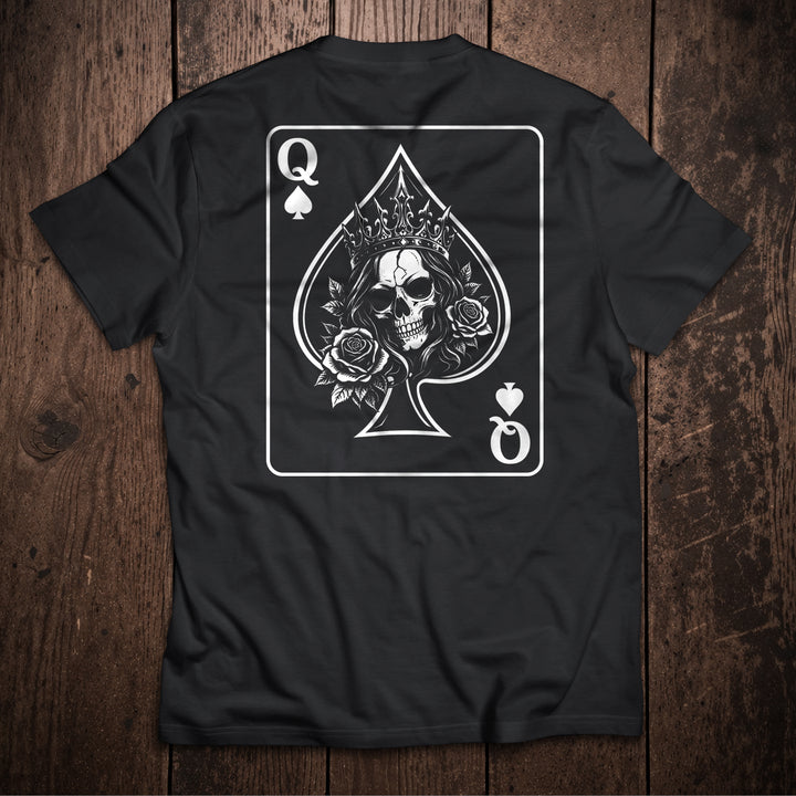 Black t-shirt flat lay on wooden surface with Queen of Spades playing card design featuring crowned skull with roses illustration