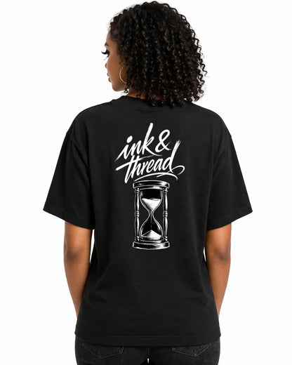 Female model showing back of black t-shirt with Ink and Thread script calligraphy and hourglass illustration on white background
