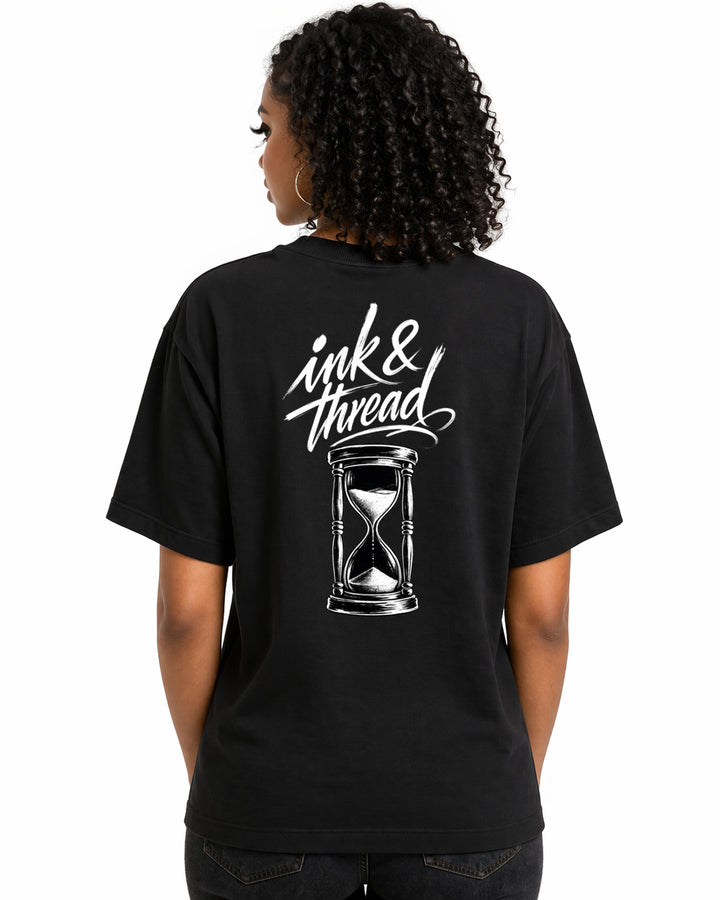 Female model showing back of black t-shirt with Ink and Thread script calligraphy and hourglass illustration on white background
