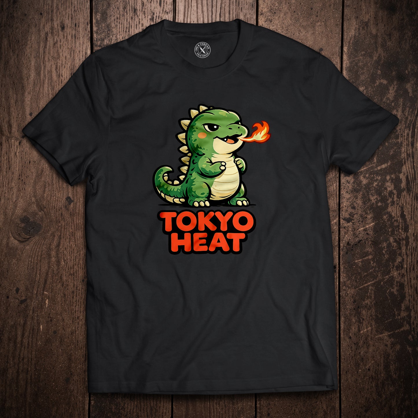 Black t-shirt flat lay on wooden surface with Tokyo Heat fire-breathing dragon cartoon illustration in bold red text