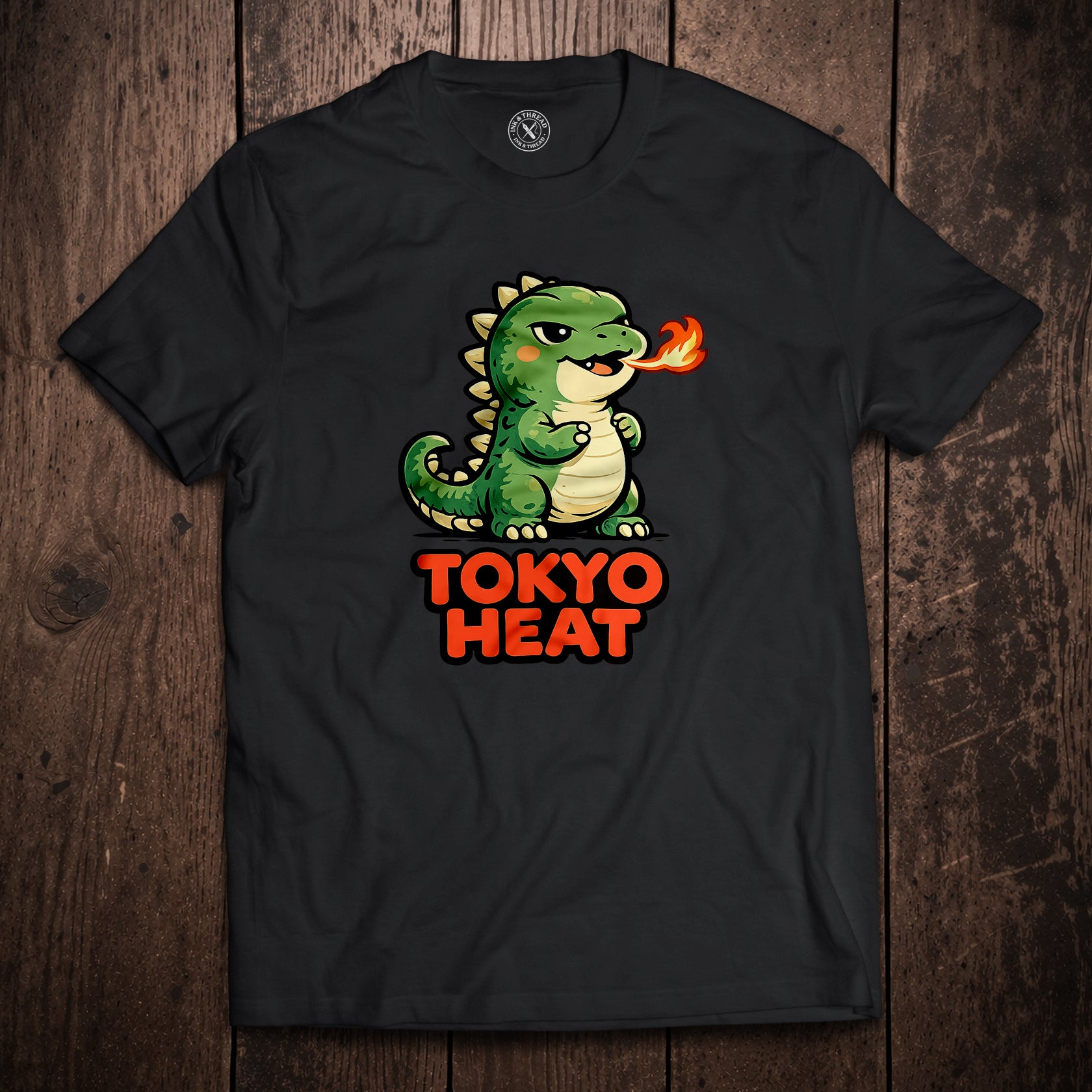 Black t-shirt flat lay on wooden surface with Tokyo Heat fire-breathing dragon cartoon illustration in bold red text