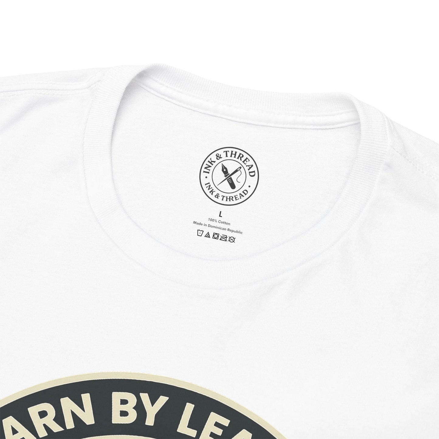 Close-up of Ink and Thread UK branded inner neck label on white t-shirt with Learn By Leaving camping graphic design and care instructions