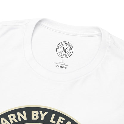 Close-up of Ink and Thread UK branded inner neck label on white t-shirt with Learn By Leaving camping graphic design and care instructions