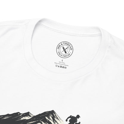 Close-up of Ink and Thread UK inner neck label on white t-shirt featuring mountain and hiker graphic, showing brand stamp size and care instructions